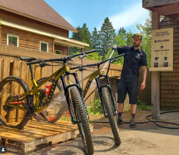 Man cleaning a mountain bike outdoors near a wooden building
